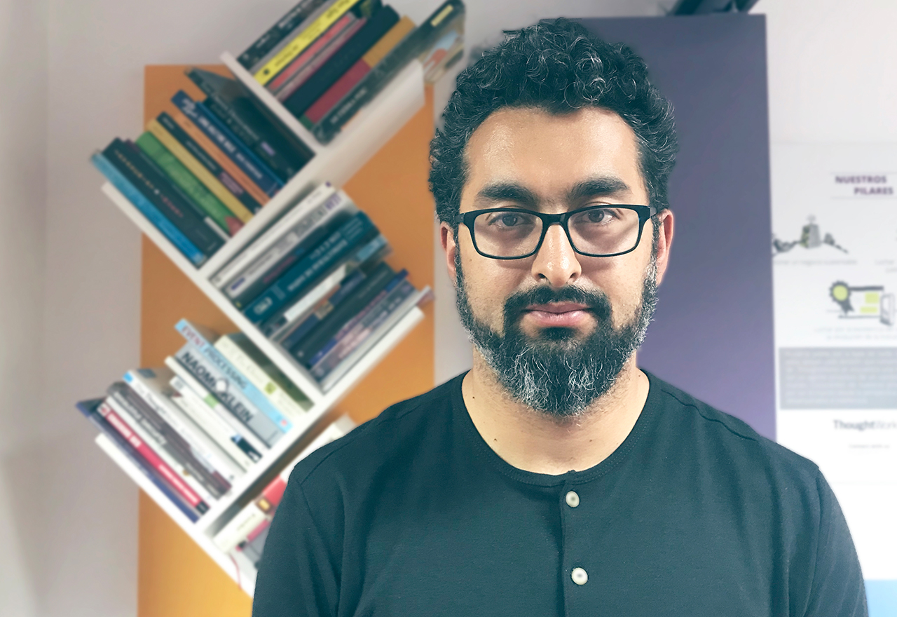 Eduardo Meneses standing in front of a bookshelf, looking directly at the camera